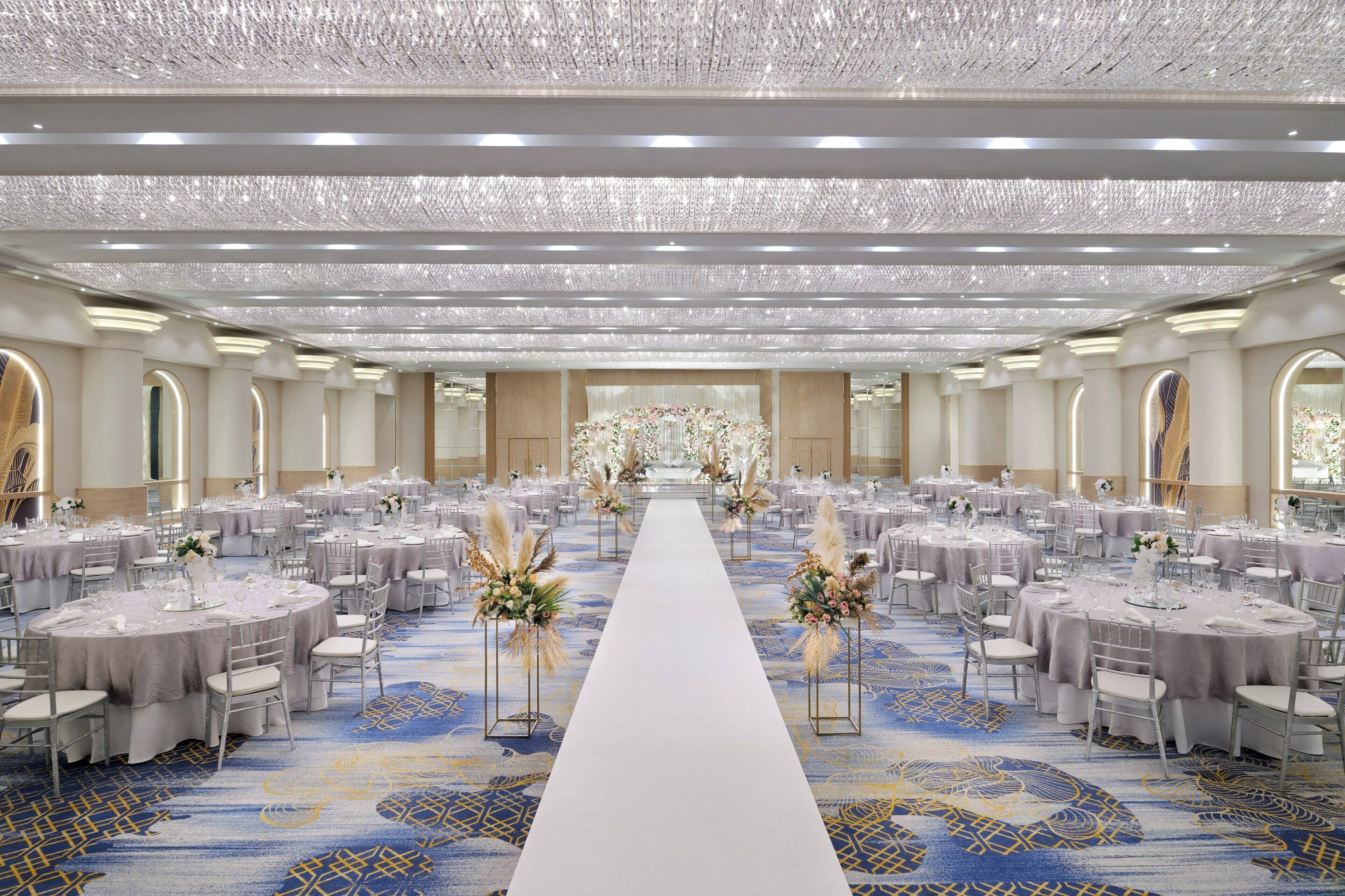 A banquet hall with round tables, a central aisle, and chandeliers.