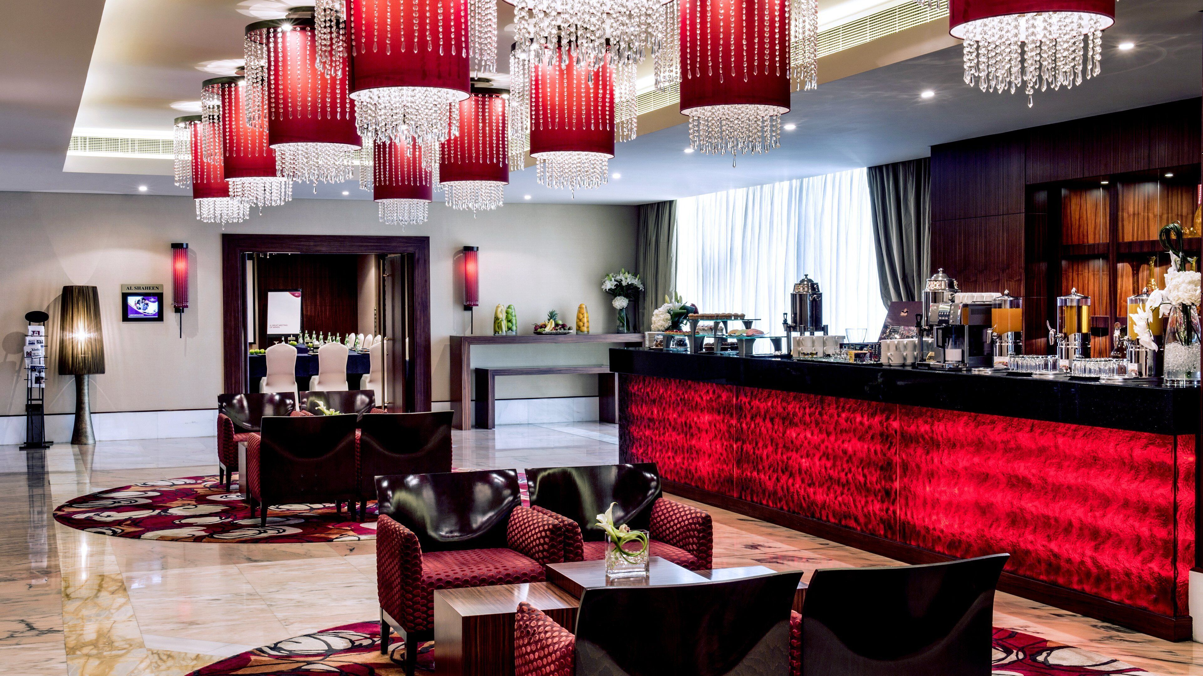 A hotel lobby with red chandeliers, a reception desk, and seating areas.