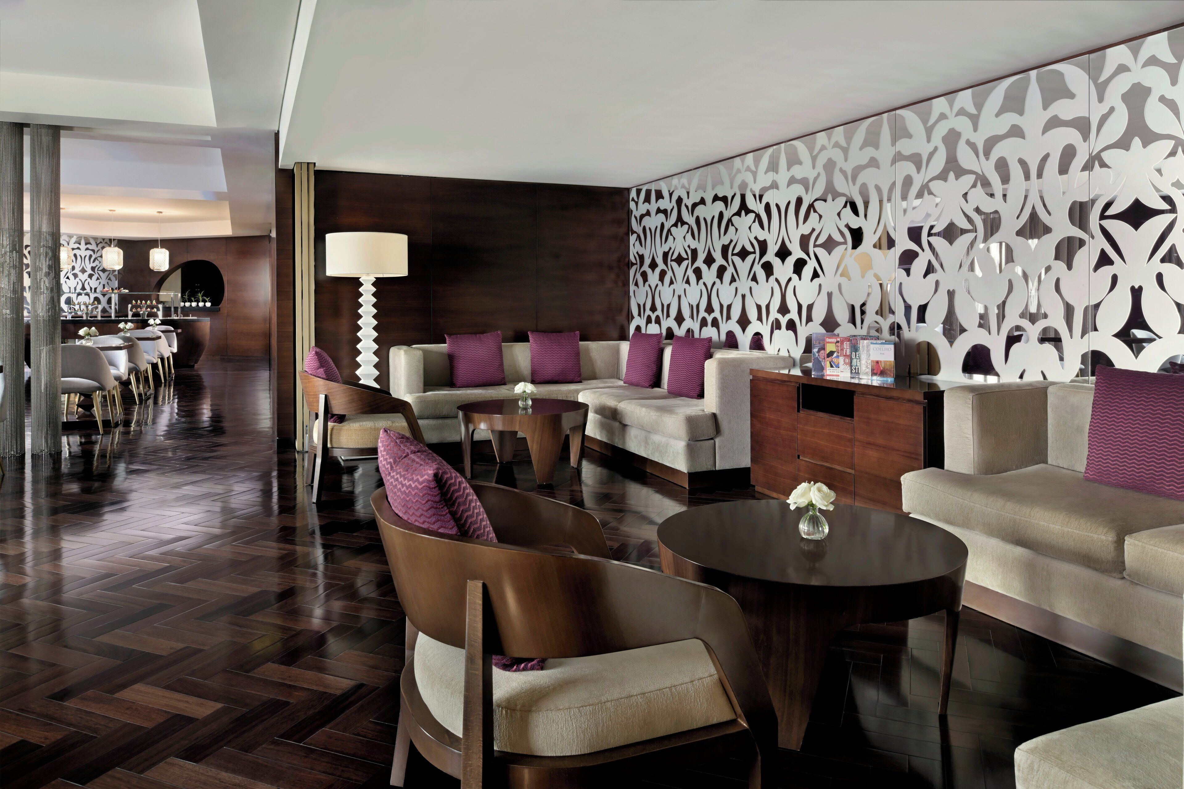 A modern hotel lobby with a herringbone wood floor, leather sofas, and a decorative wall panel.