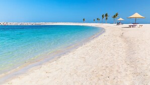 A beach with clear turquoise water, white sand, and palm trees. There are beach umbrellas and lounge chairs. - Crowne Plaza Dubai Deira by IHG (Dubai)