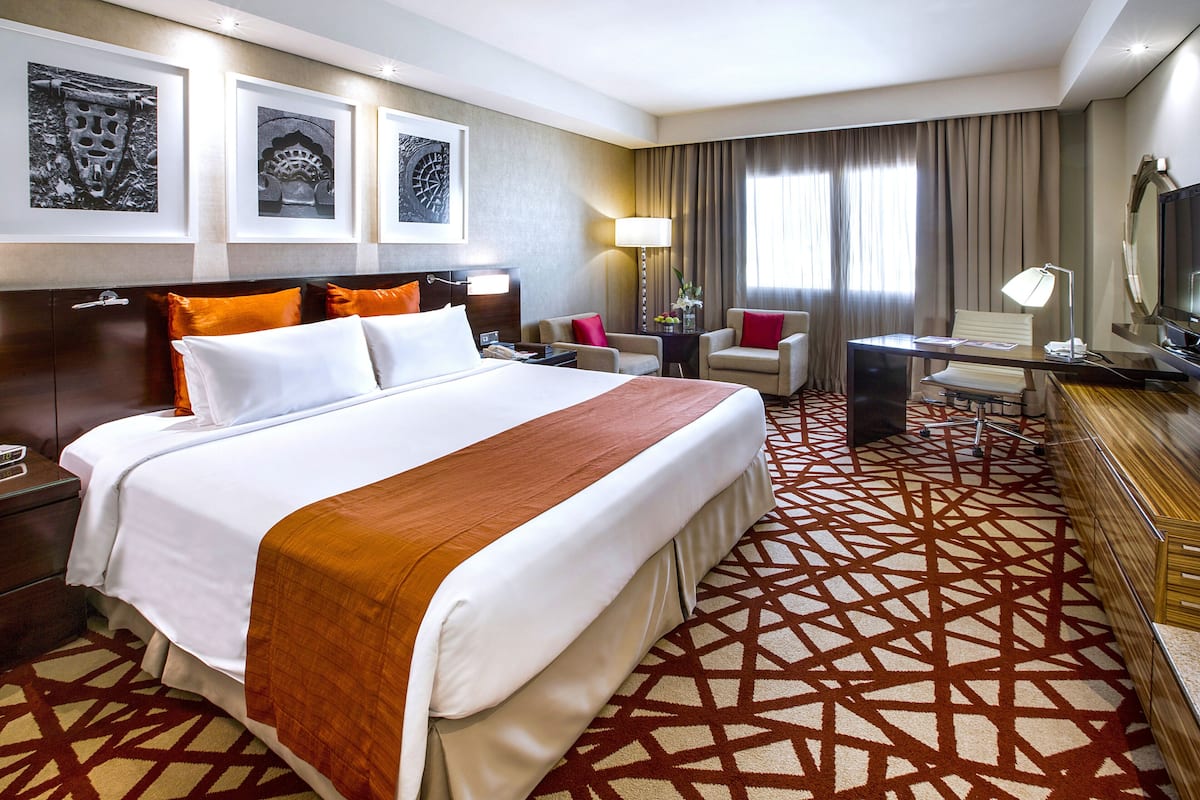Une chambre d’hôtel avec un grand lit, un bureau, une chaise, une télévision et des œuvres d’art accrochées au mur.