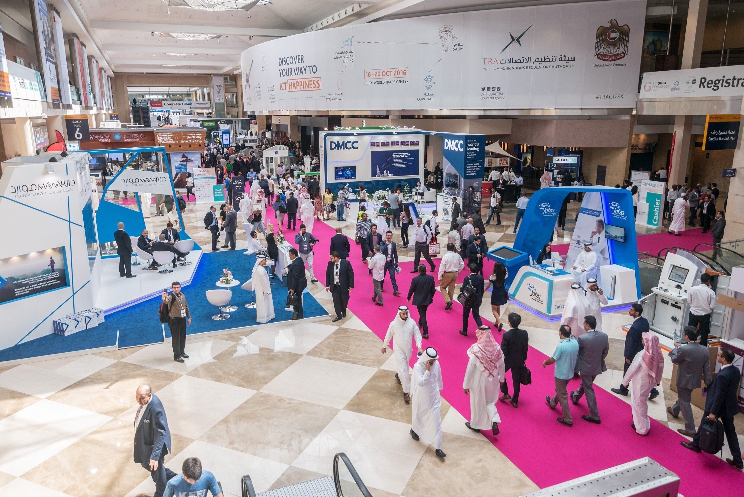 A busy indoor event with people walking on a checkered floor, booths, and banners.