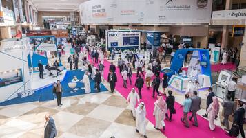A busy indoor event with people walking on a checkered floor, booths, and banners.