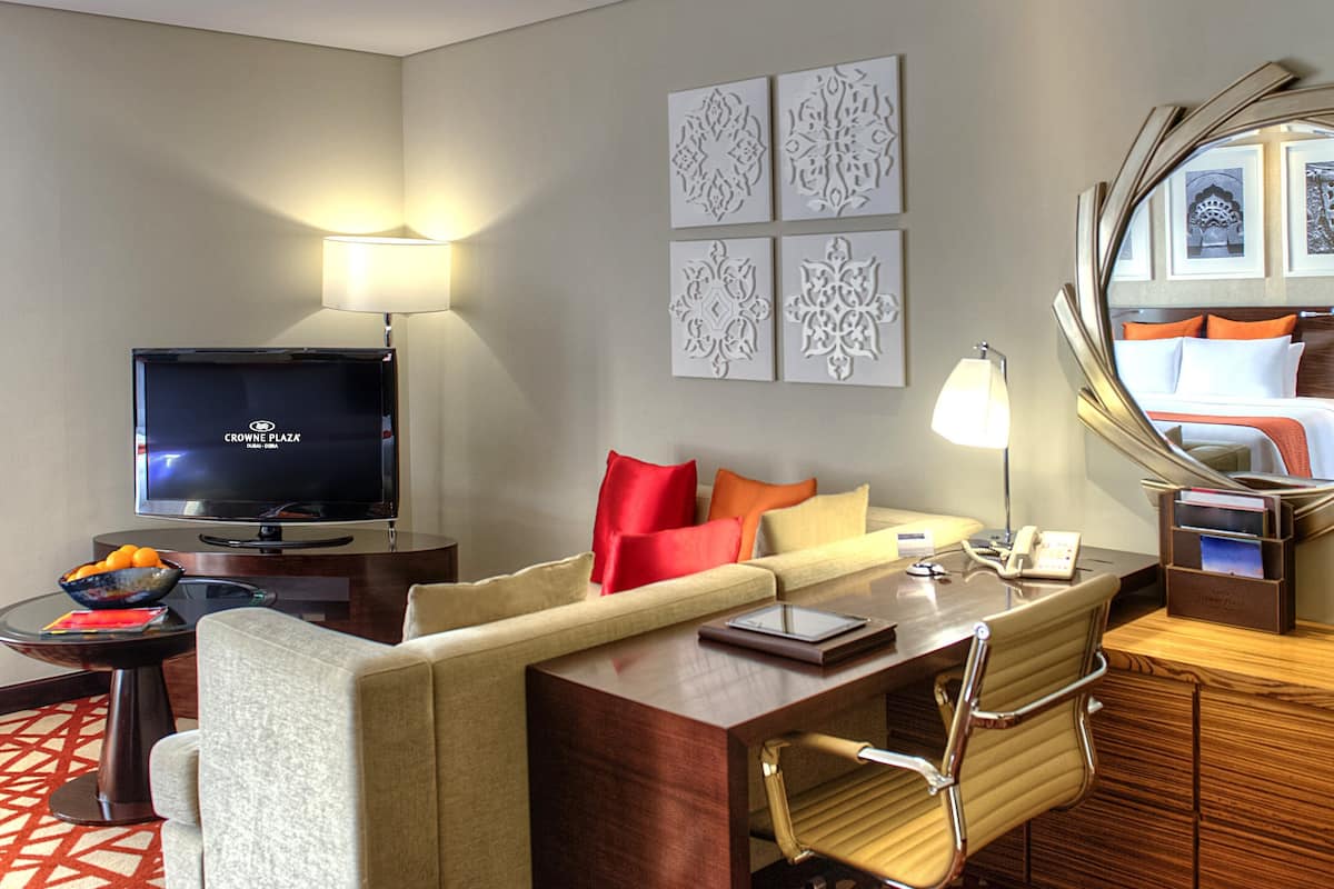Une chambre d’hôtel équipée d’une télévision, d’un canapé, d’un bureau, d’une chaise, d’un miroir et d’œuvres d’art accrochées aux murs.