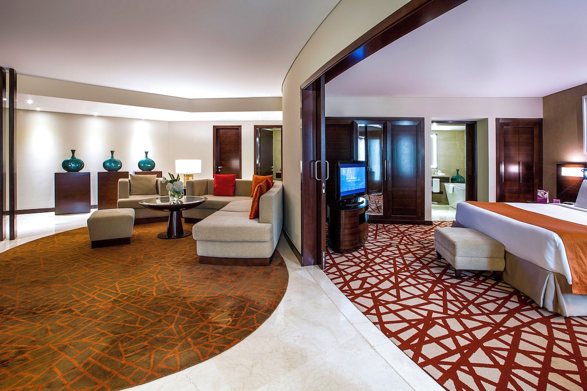 Ein Hotelzimmer mit Sitzecke, Fernseher, Bett und einem durch eine offene Tür einsehbaren Badezimmer.