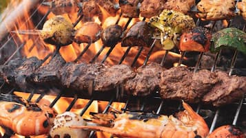 Una parrilla con carnes y verduras cocinándose a fuego abierto.