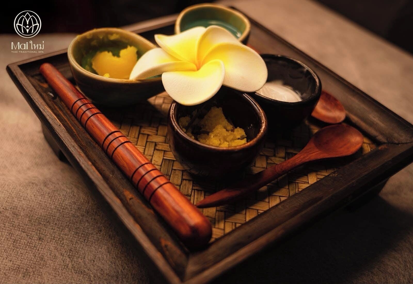 A tray with two bowls containing yellow substances, a white flower, and a wooden spoon.