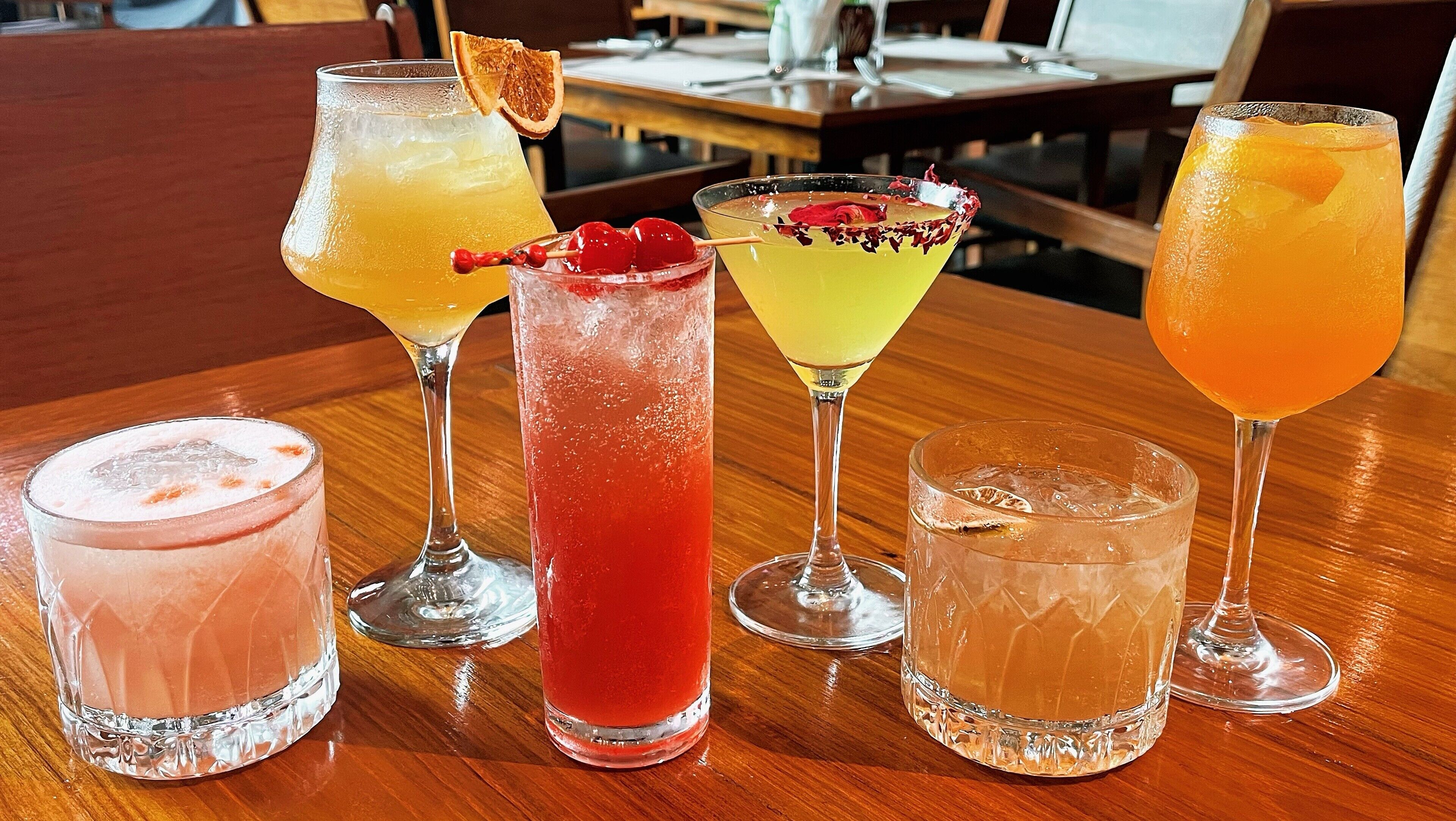 A variety of cocktails on a wooden table in a restaurant setting.