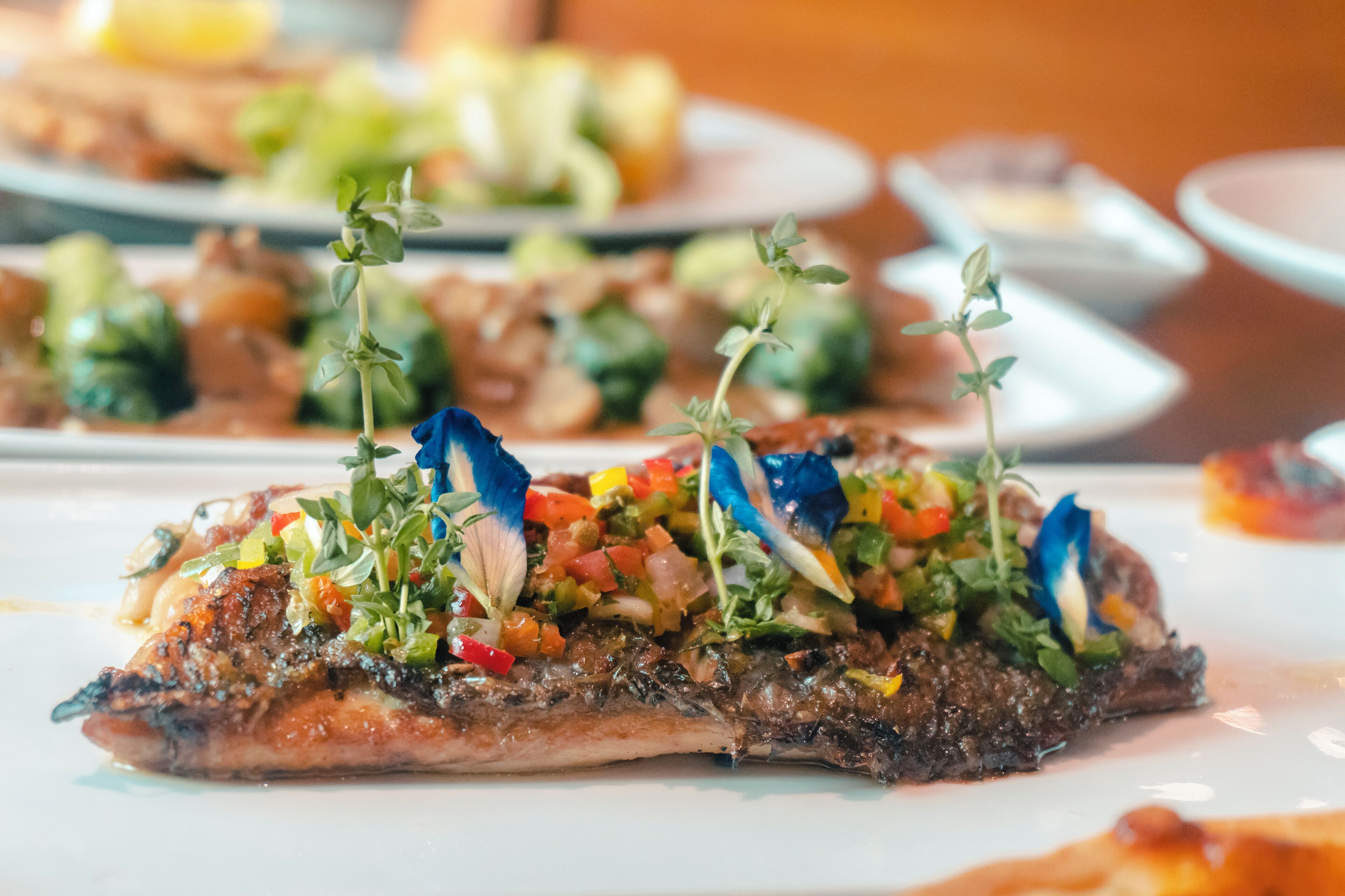 A plate of food with a grilled fish topped with colorful vegetables and herbs.