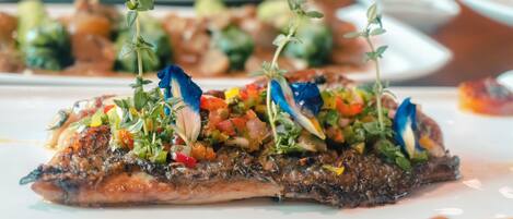A plate of food with a grilled fish topped with colorful vegetables and herbs.
