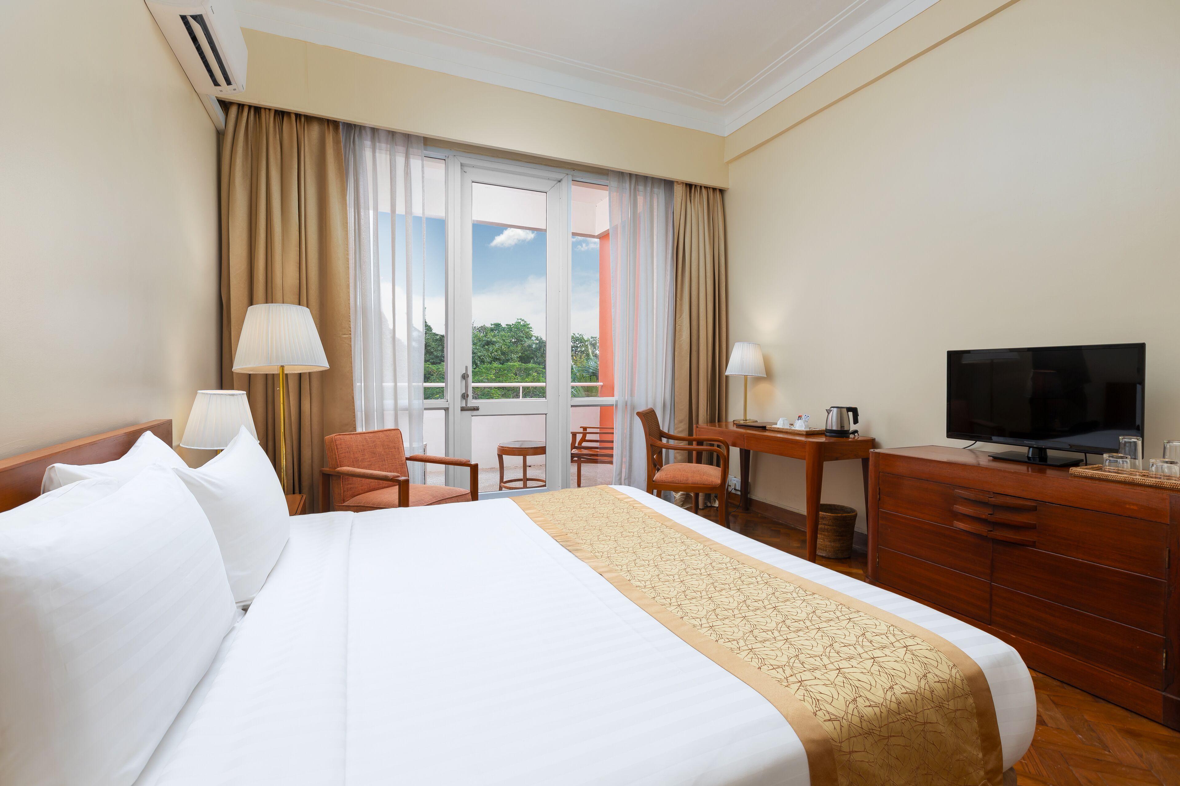 Una habitación de hotel con una cama grande, un escritorio con silla, televisión y vistas al exterior.