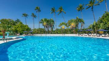 Relax by the pool surrounded by lush greenery and palm trees, with lounge chairs and umbrellas at your disposal.
