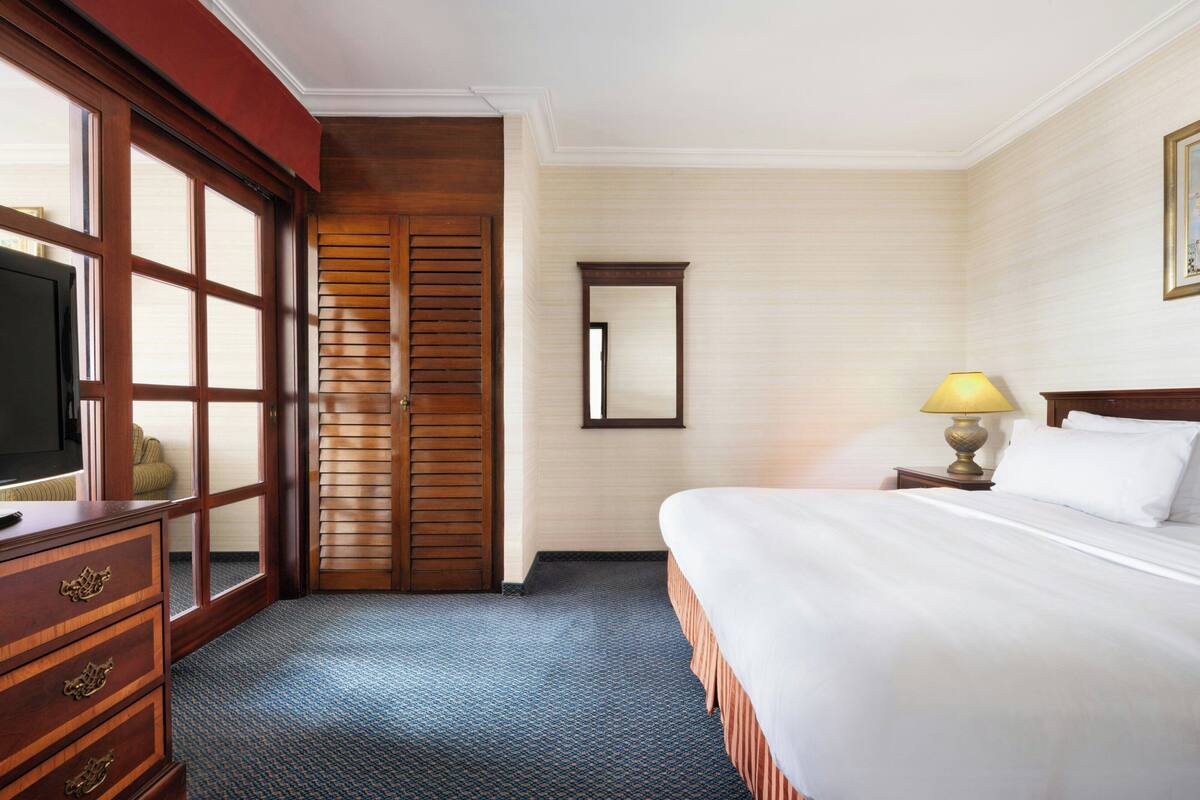 A hotel room with a bed, a dresser, a television, a lamp, and a window with blinds.