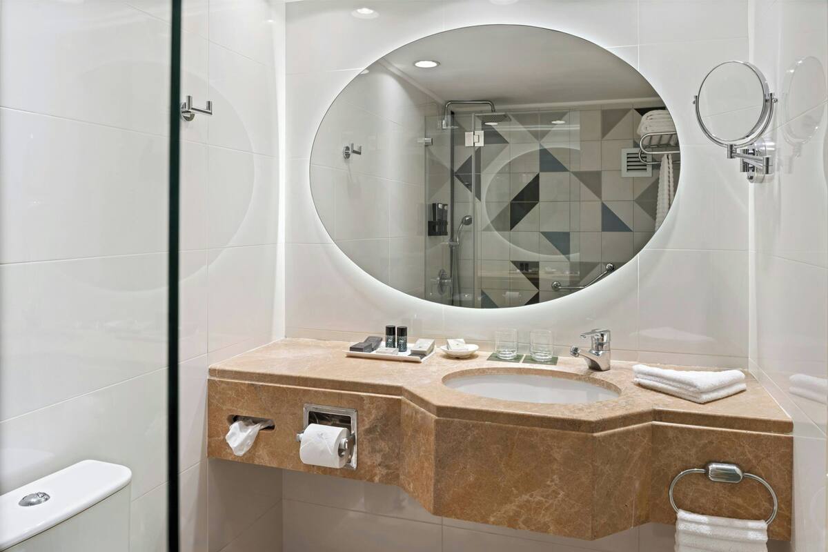 A modern bathroom with a large mirror, a sink, and a toilet.