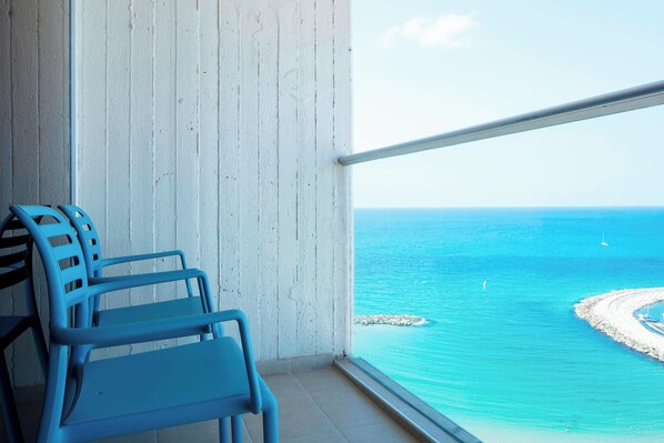 A balcony with two blue chairs, a white wall, and a view of the ocean with a small island and boats.