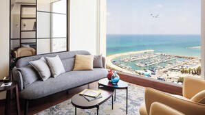 Un salon moderne avec un canapé gris, une petite table basse et une vue sur une marina et une plage.