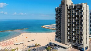 Un hôtel de grande hauteur doté de nombreux balcons offrant une vue sur une plage et un port de plaisance.