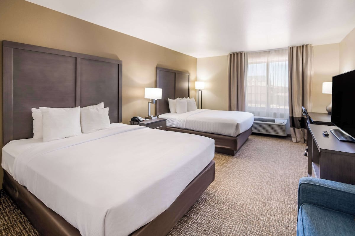 A hotel room with two beds, a desk, a TV, and a large window with curtains.