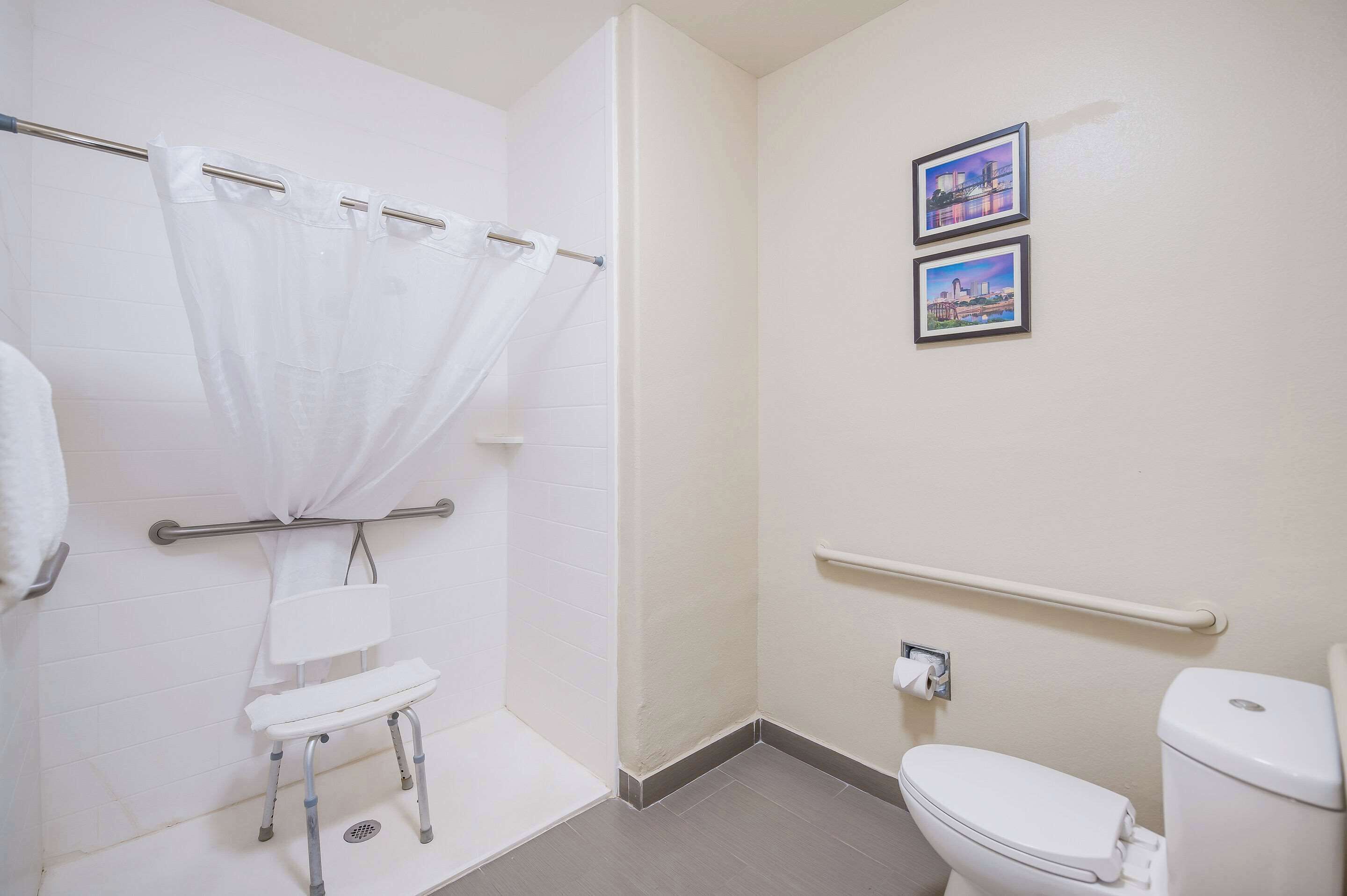Un baño con ducha, inodoro y barra de apoyo.