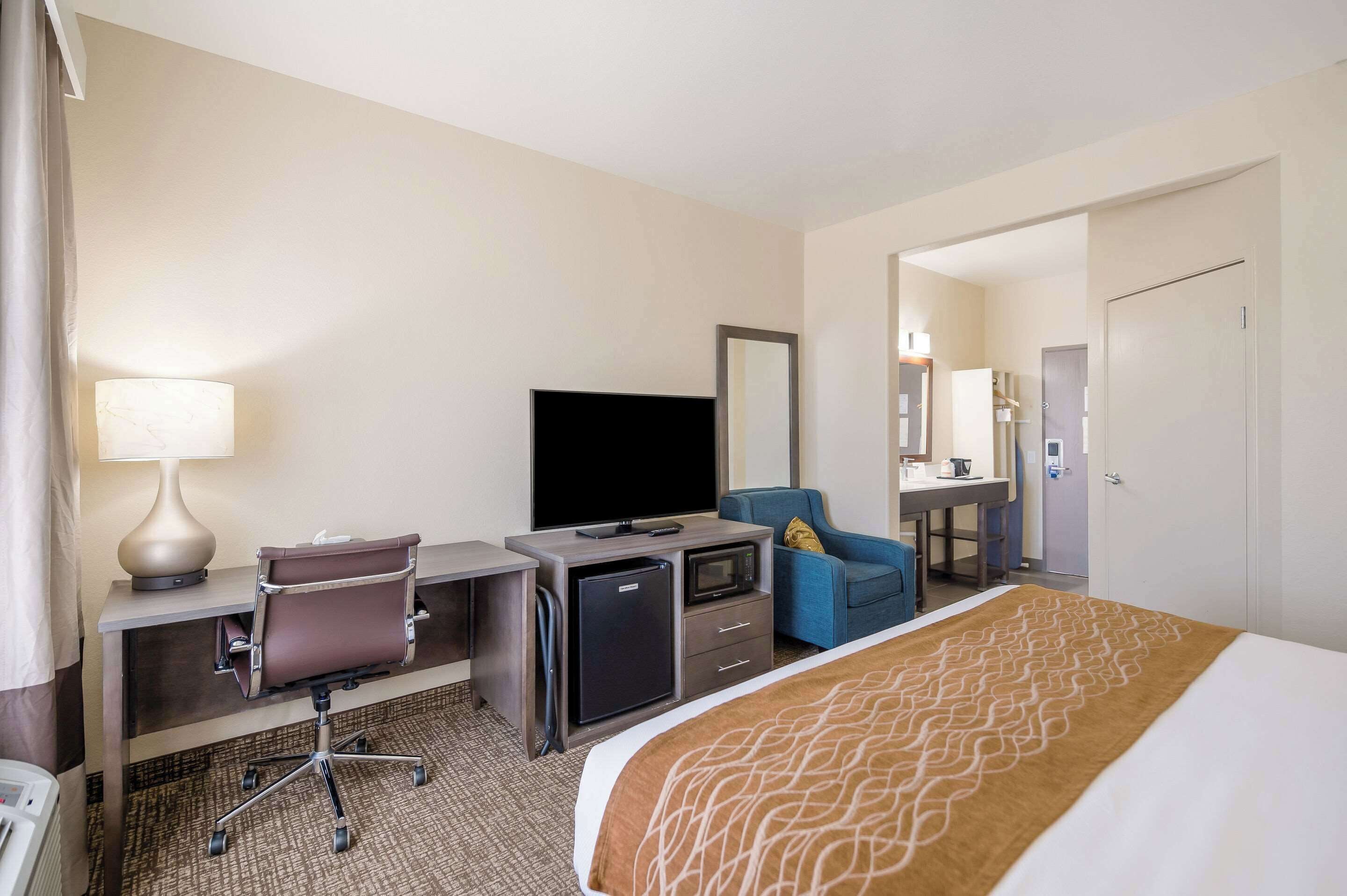 A hotel room with a bed, desk, chair, television, and a small refrigerator.