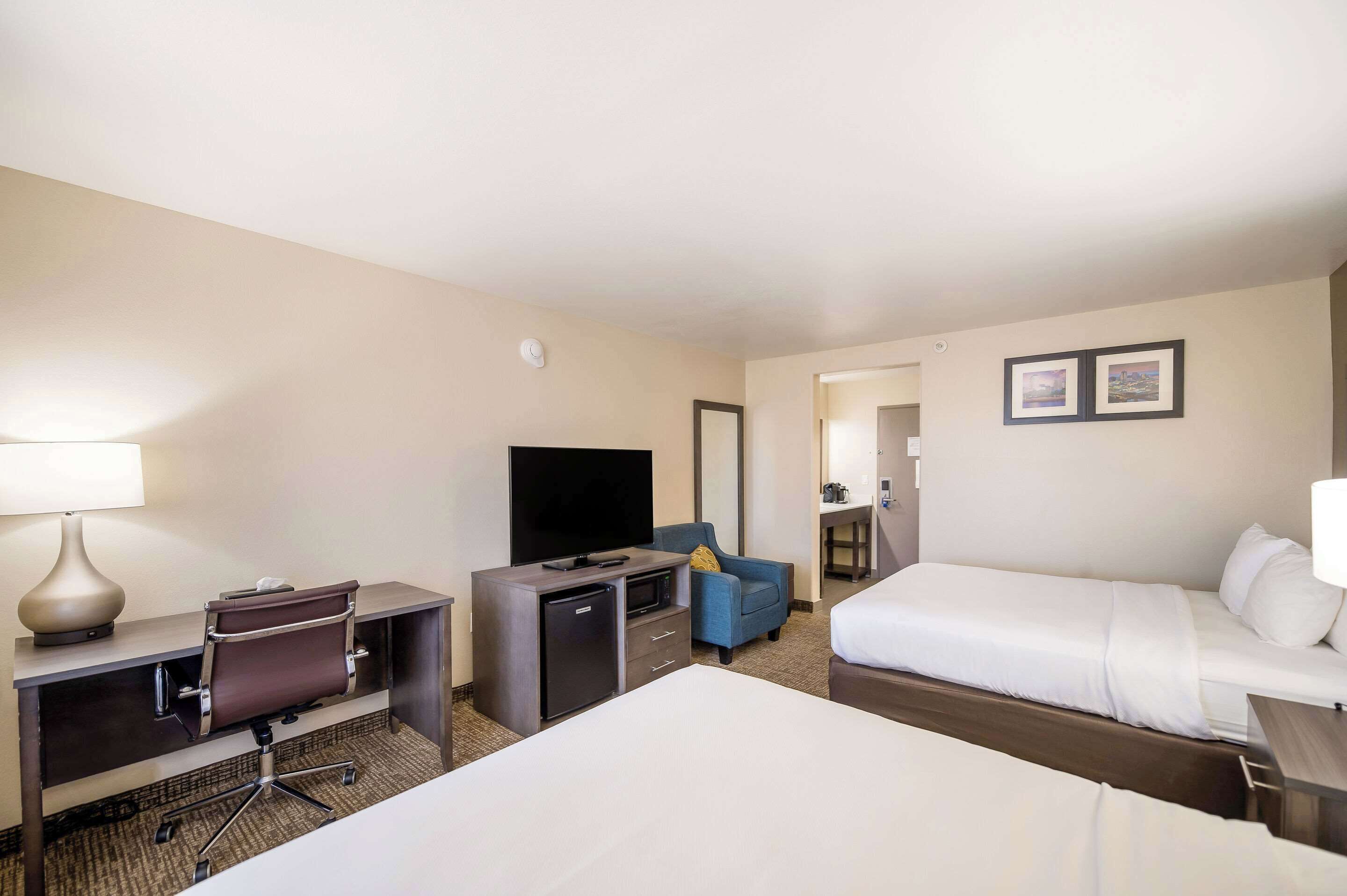 A hotel room with a bed, a desk with a computer, a television, a chair, and a small refrigerator.