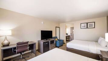 A hotel room with a bed, a desk with a computer, a television, a chair, and a small refrigerator.