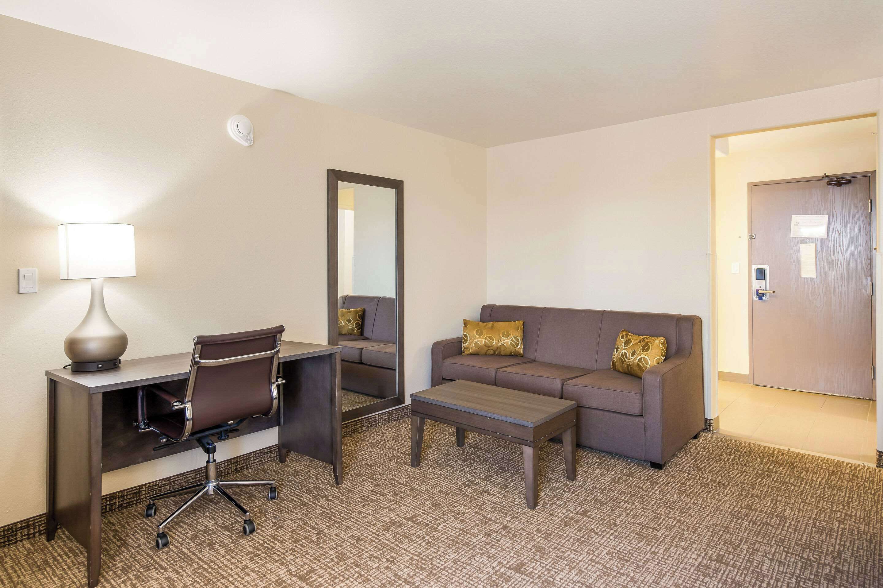 A hotel room with a desk, chair, sofa, and a small table.