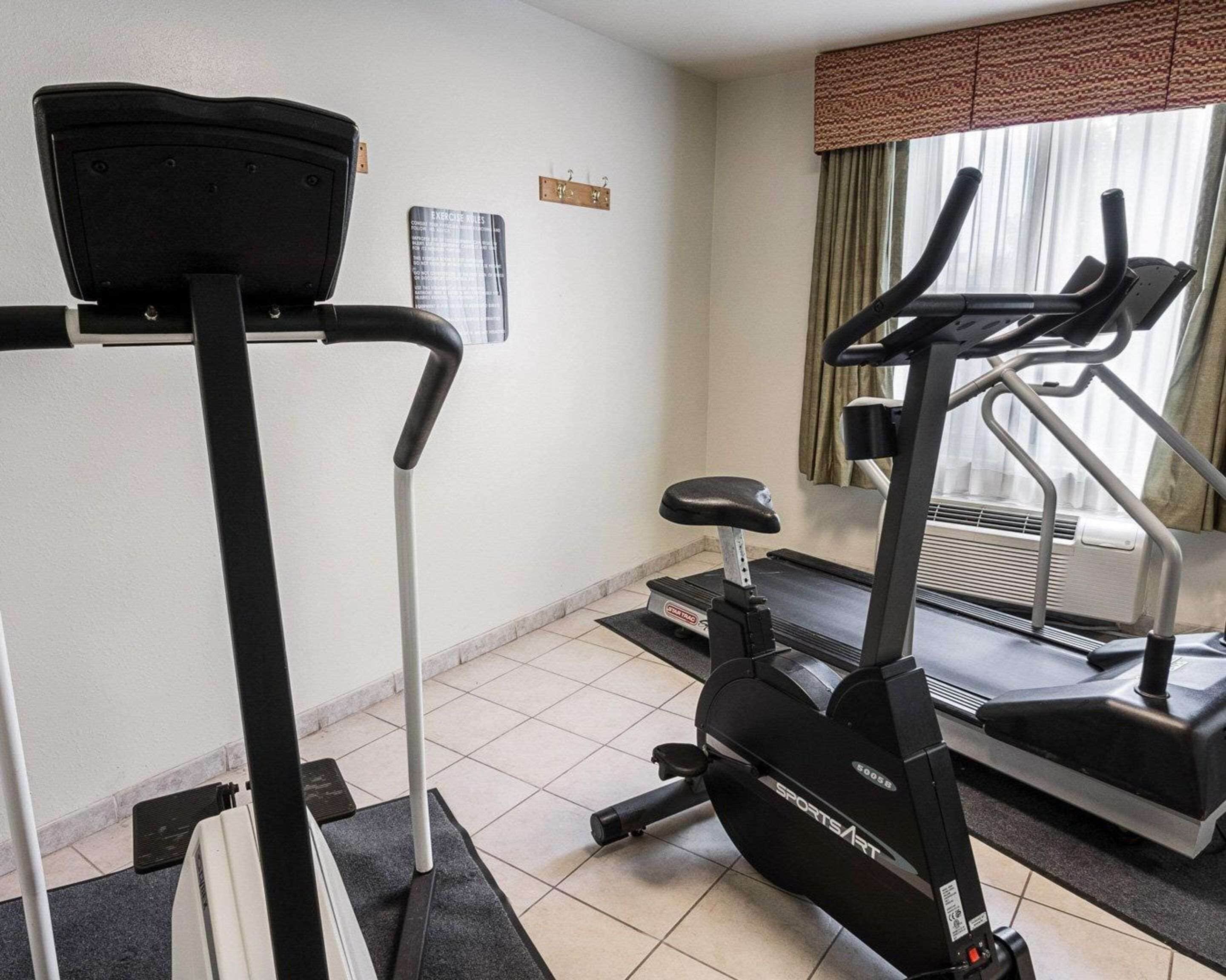 A gym with a treadmill, elliptical, and a stationary bike. There is a sign on the wall and a window with curtains.
