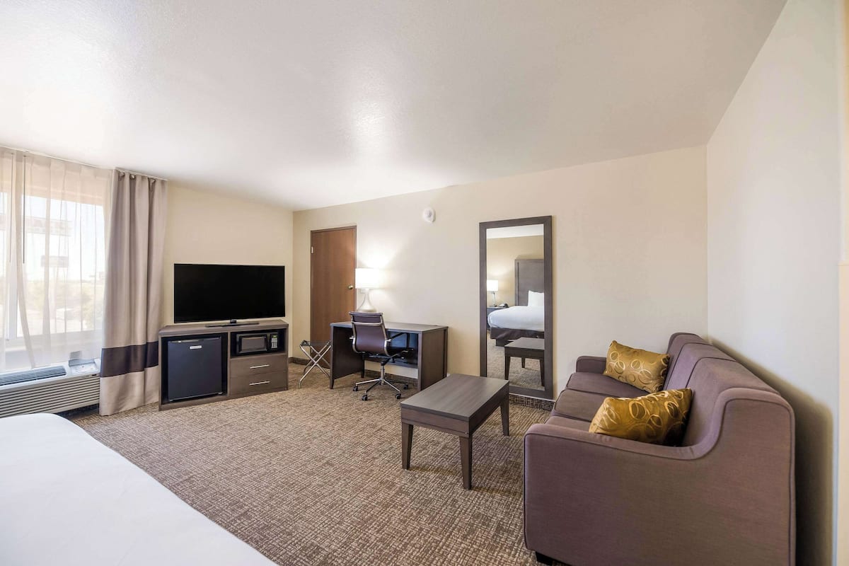 A hotel room with a bed, a desk with a chair, a television, a sofa, and a small table.