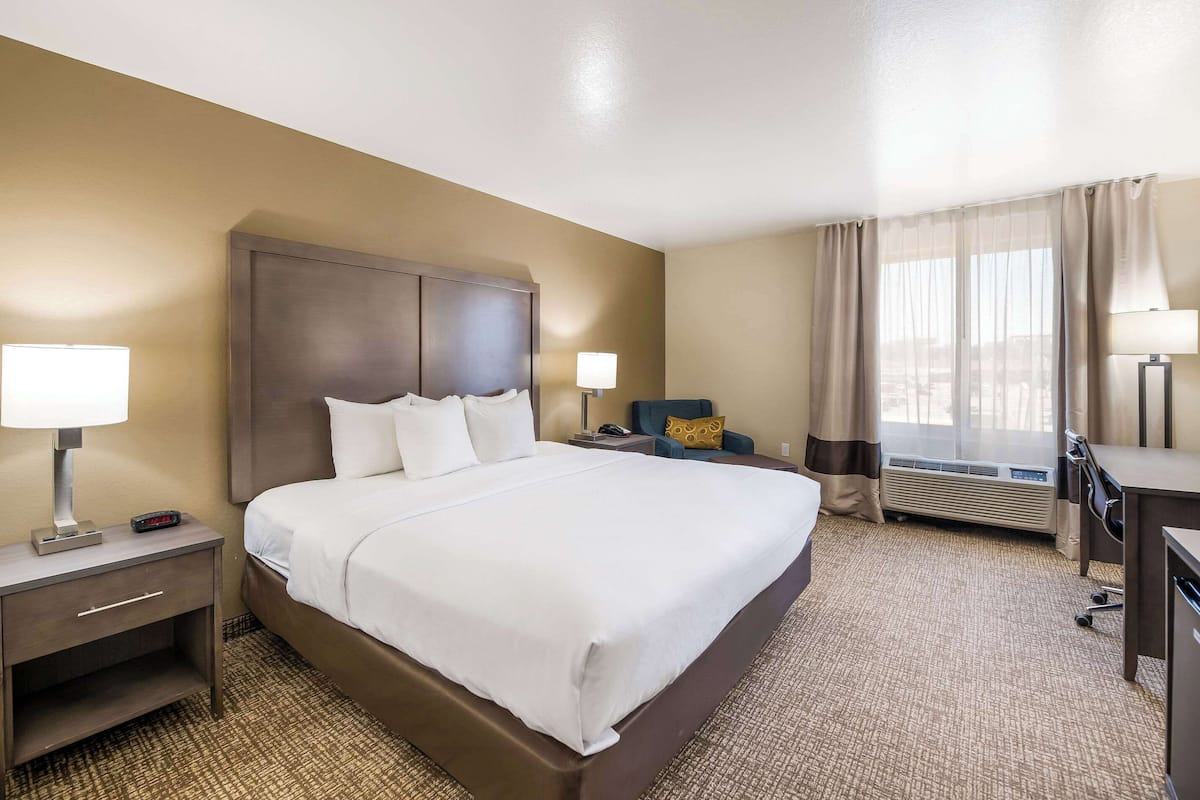 A hotel room with a large bed, two bedside tables with lamps, a desk, and a chair.