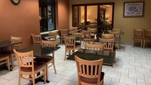 A dining area with multiple tables and chairs, a clock on the wall, and a large window with a view of the outside. - Baymont by Wyndham Asheville/Biltmore Village (Asheville)