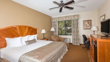 A hotel room with a large bed, a desk with a computer, a chair, a television, and a ceiling fan.
