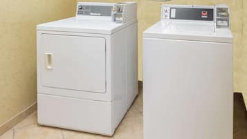 Two white front-loading washing machines in a room with beige patterned wallpaper and tiled flooring.