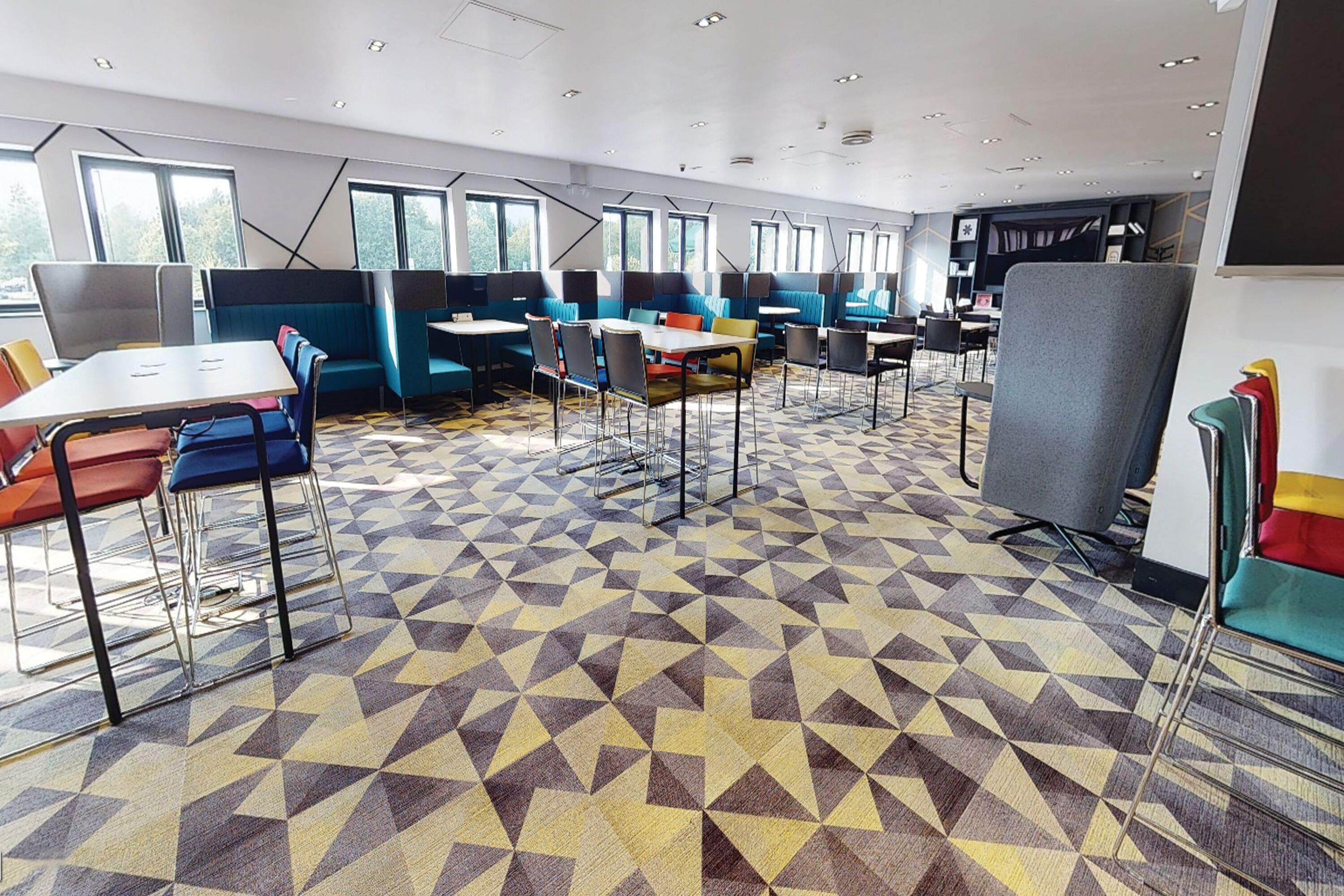 A modern dining area with geometric patterned flooring, multiple seating arrangements including booths and tables, and large windows providing natural light.