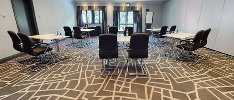 Un salón de conferencias con alfombra geométrica, varias mesas y sillas dispuestas para reuniones.