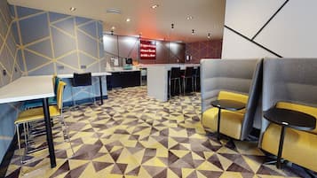 A modern hotel lobby with geometric patterned flooring, a reception desk, and seating areas.