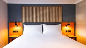 A modern hotel room with a large bed, two bedside tables, and a wooden headboard. - Village Hotel Coventry (Coventry)