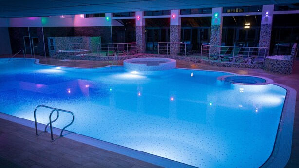 An indoor swimming pool with a tiled deck, a hot tub, and a seating area with chairs and a table. - Village Hotel Coventry (Coventry)