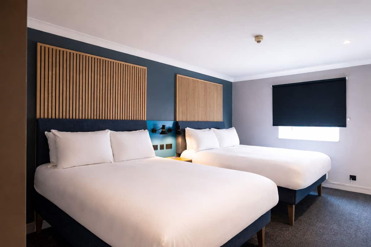 A hotel room with two beds, a window, and a wall-mounted light fixture.