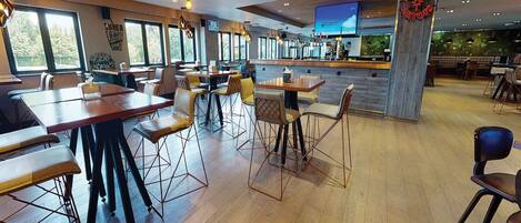 A spacious restaurant with wooden tables and chairs, a bar area, and large windows offering views.