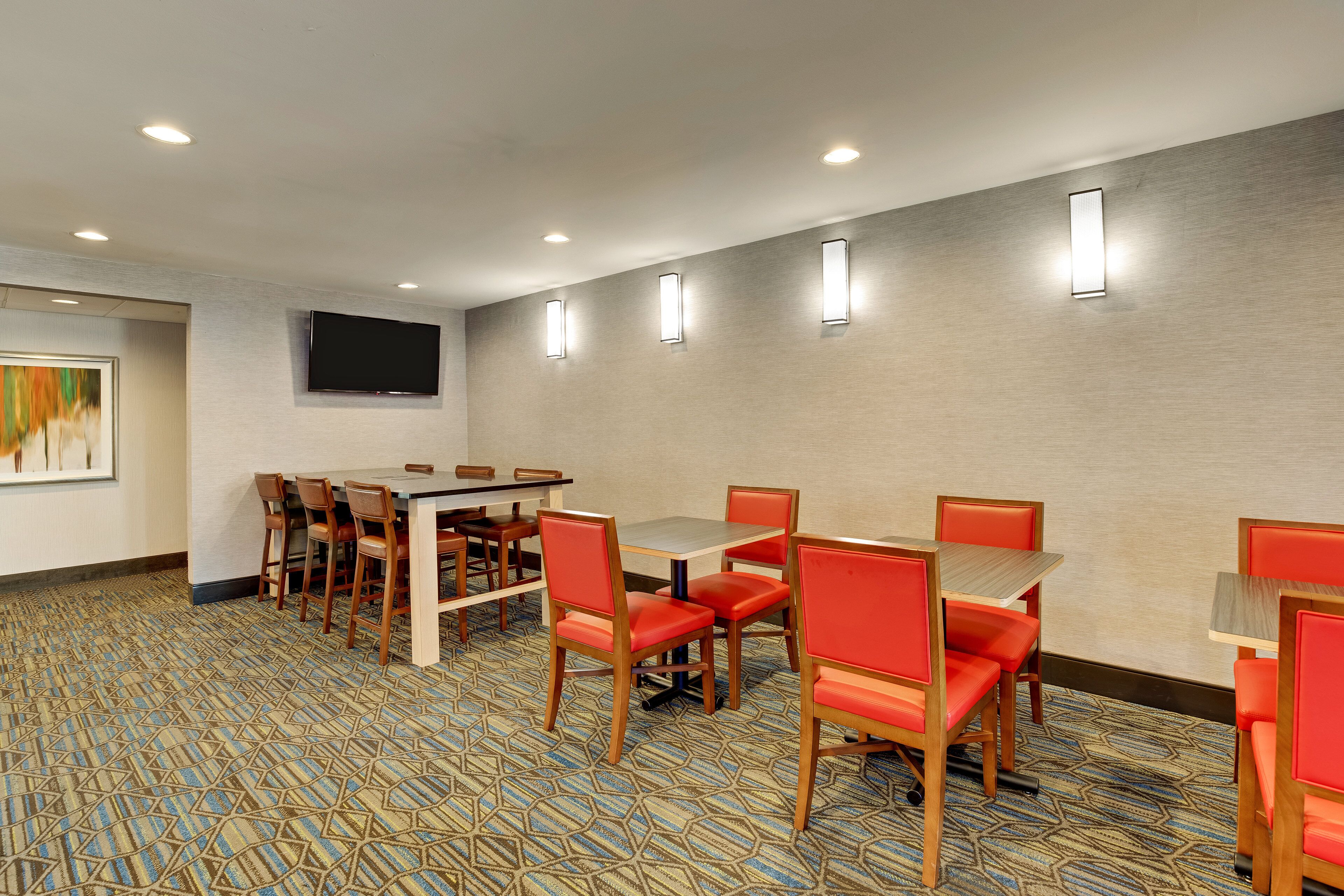 A conference room with a large table and several chairs, a flat-screen TV mounted on the wall, and patterned carpet.