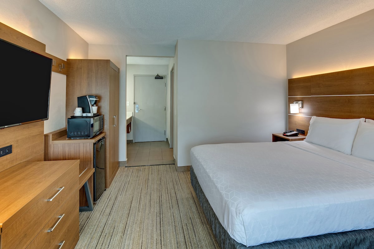 A hotel room with a large bed, a TV, a desk with a microwave, and a small cabinet.