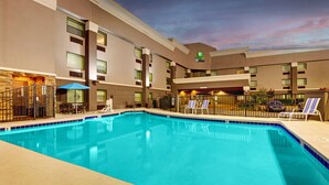 A hotel pool area with a clear blue pool, lounge chairs, and a stone wall. - Holiday Inn Express W-I40/Whitebridge Road by IHG (Nashville)