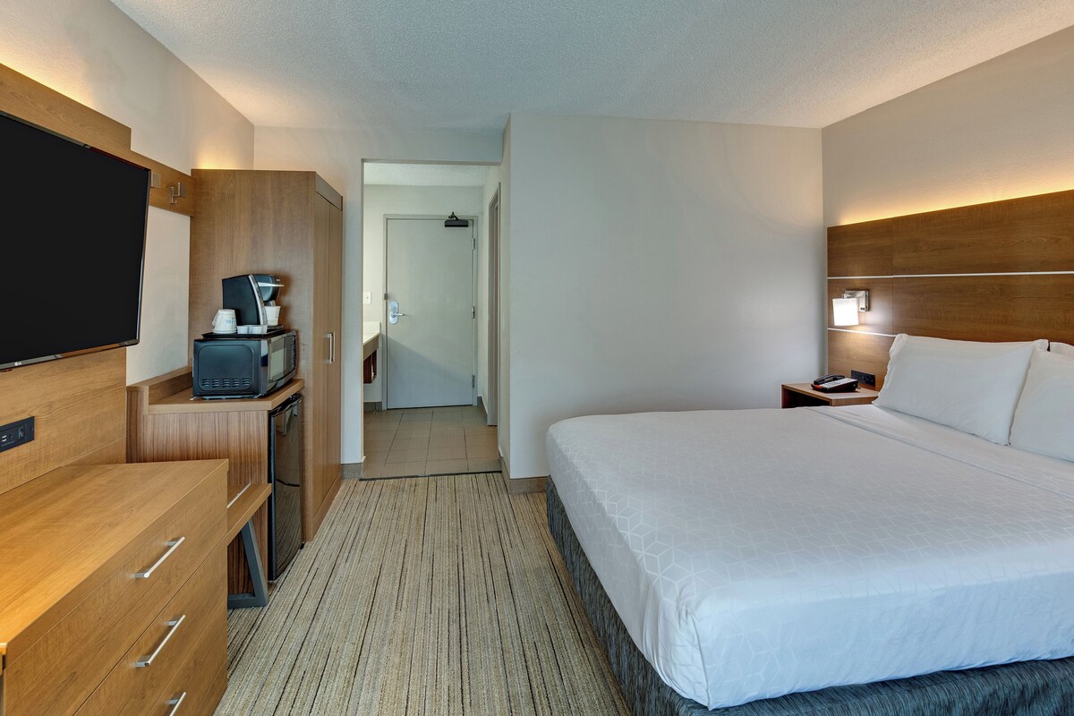 A hotel room with a large bed, a TV, a desk with a microwave, and a small cabinet.