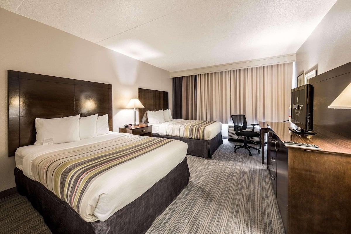 Une chambre d’hôtel avec deux lits, un bureau, une chaise, une télévision et une lampe.