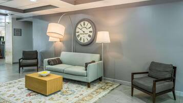 A modern lobby with a grey sofa, two armchairs, a wooden coffee table, and a large wall clock.