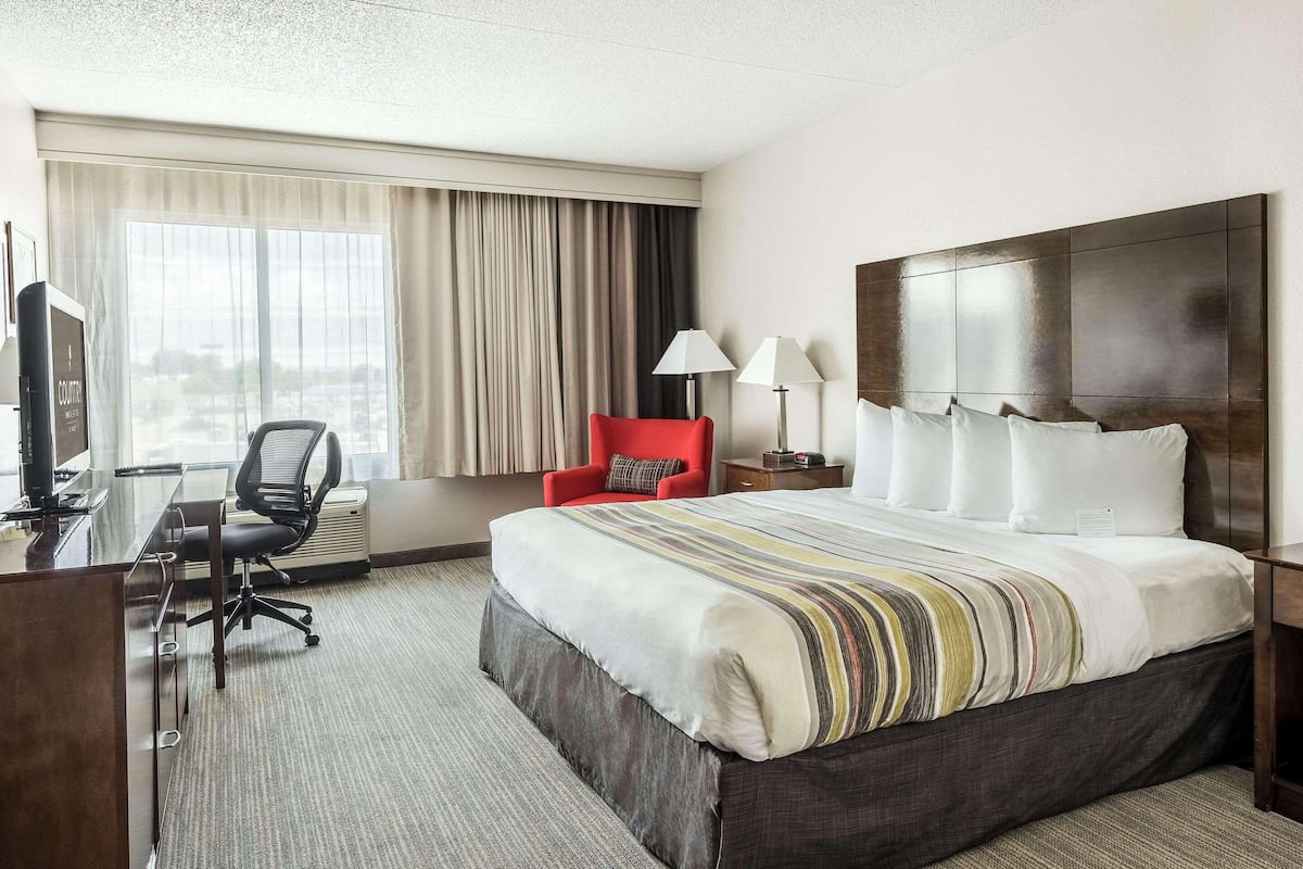 Une chambre d’hôtel avec un grand lit, un bureau avec une chaise, un fauteuil rouge et un téléviseur.