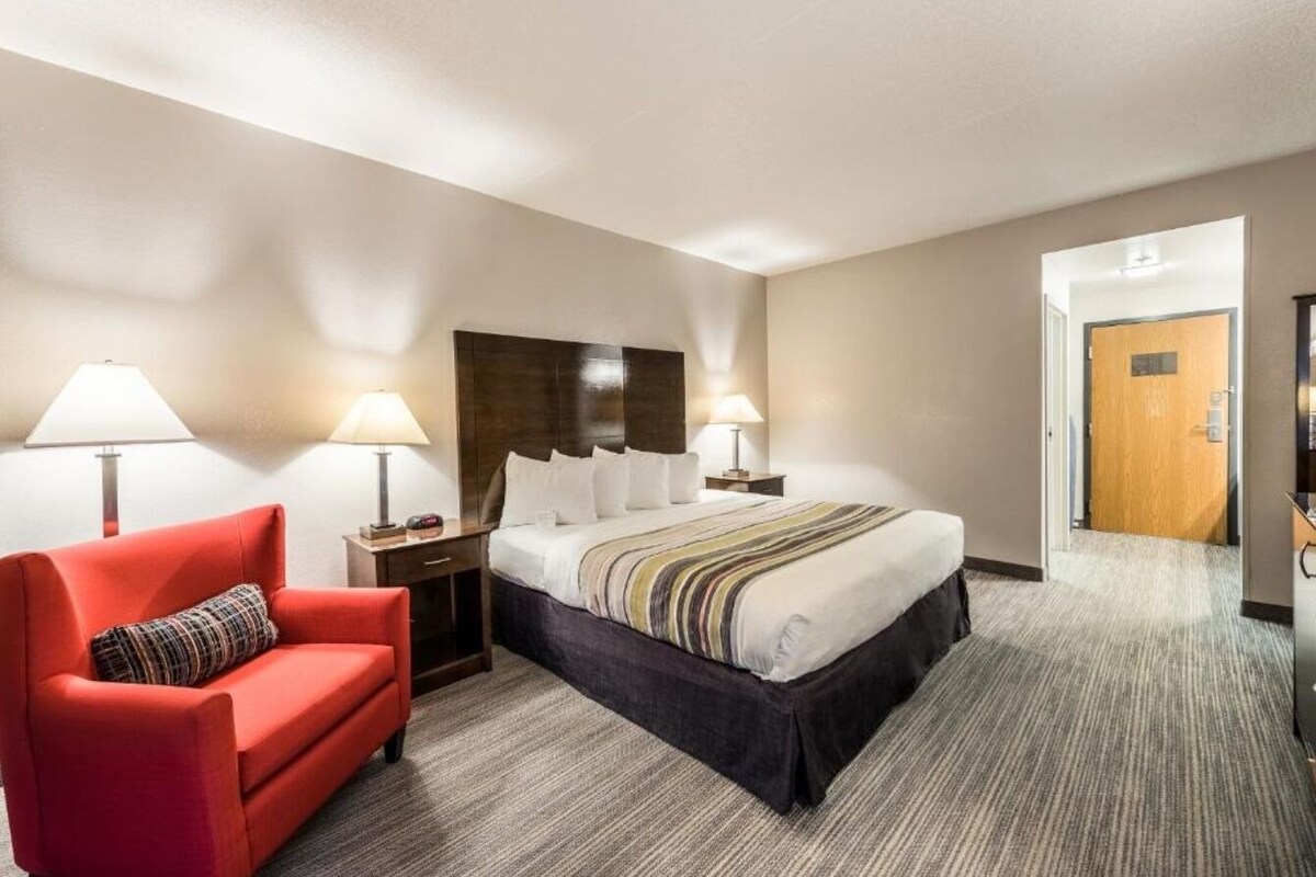 Een hotelkamer met een bed, een rode fauteuil, twee bedlampen, een houten hoofdeinde en een vloerbedekking.