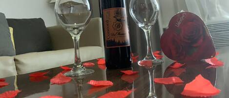 A table with a bottle of wine, two glasses, and red rose petals.