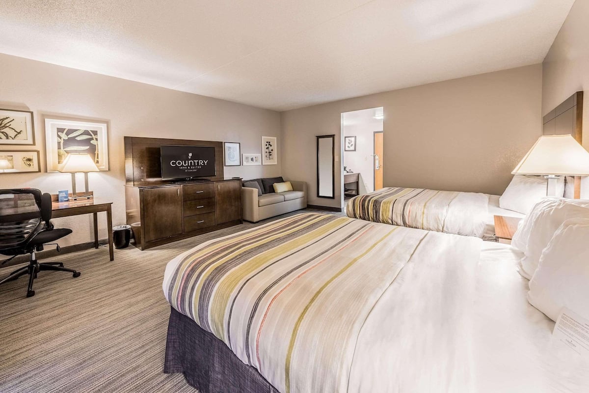 Une chambre d’hôtel avec un lit, un bureau, une chaise, une télévision et un miroir.